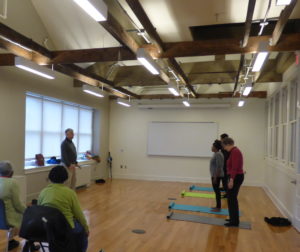 Mr. Kramer teaching qigong energy healing techniques to a class, while other people are sitting watching.