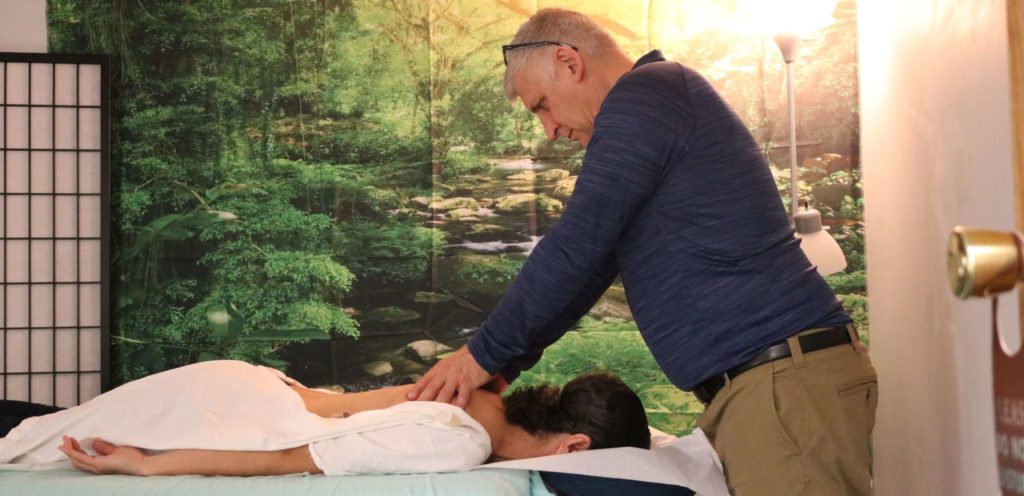 Mr. Kramer performing qigong energy healing on a woman who is faced down on a table.