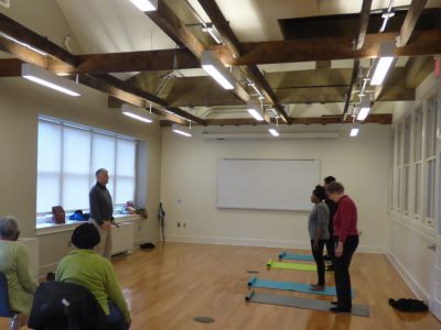 Mr. Kramer teaching qigong energy healing techniques to a class, while other people are sitting watching.